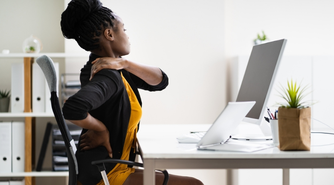 woman holding neck and back at desk