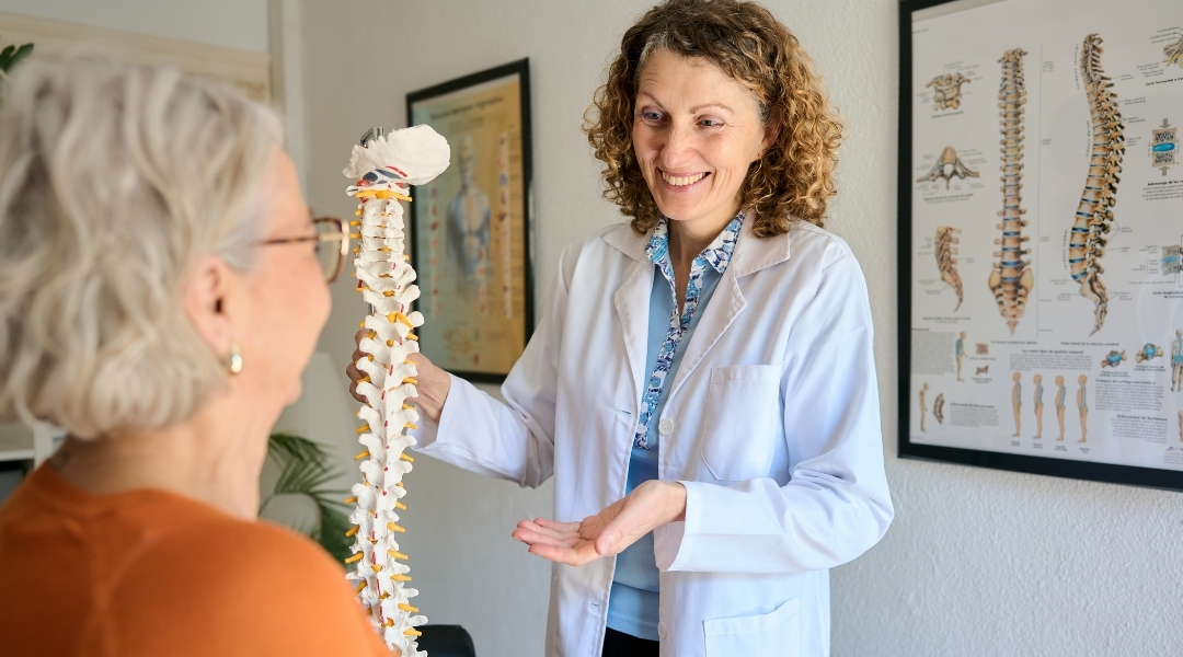 Chiropractor explaining what to expect before a first adjustment using a spine model during an initial consultation.